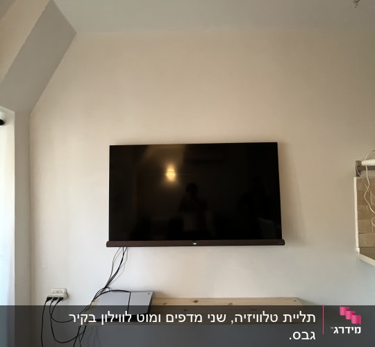 טלוויזיה תלויה על קיר עם מדף עץ וכבלים